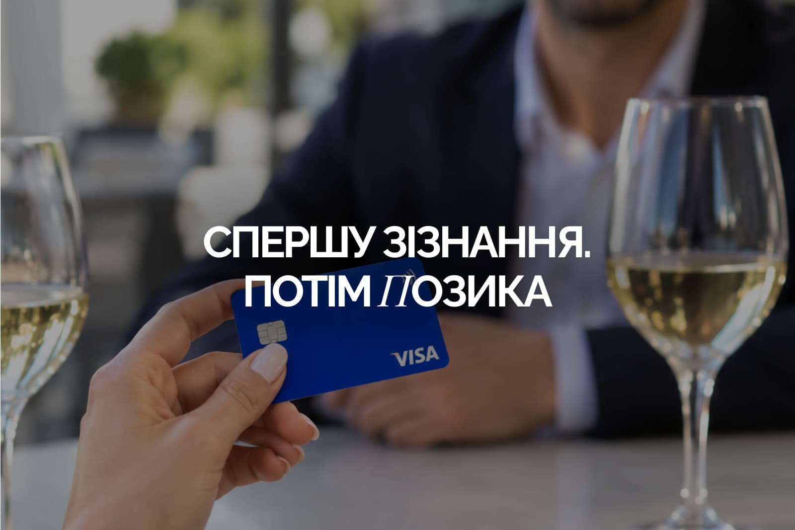 Жіноча рука тримає синю банківську картку над столиком у кафе з двома келихами, чоловік у піджаку навпроти не в фокусі, напис «Спершу зізнання. Потім позика»
